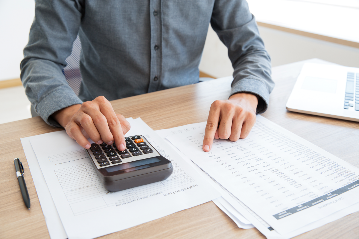 Eine Person in einem Hemd nutzt einen Taschenrechner und überprüft Dokumente, symbolisch für Finanzmanagement, Kalkulationen und präzise Budgetplanung.