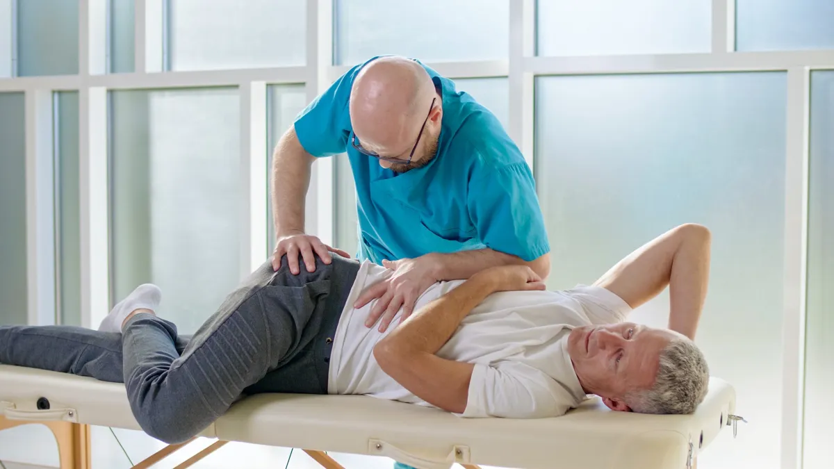 Physiotherapeut behandelt einen erwachsenen Mann auf einer Liege in einer modernen Klinik.