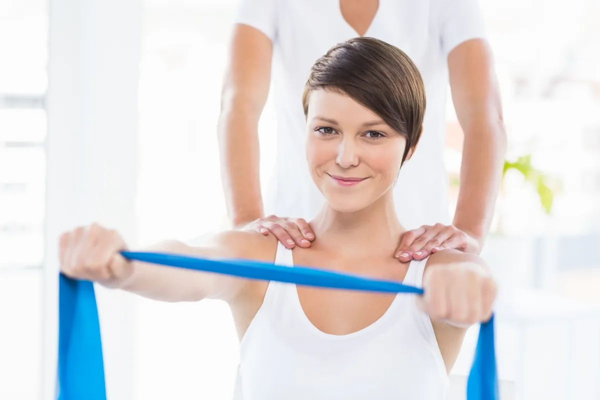 Eine junge Frau trainiert mit einem Widerstandsband unter der Anleitung eines Physiotherapeuten.